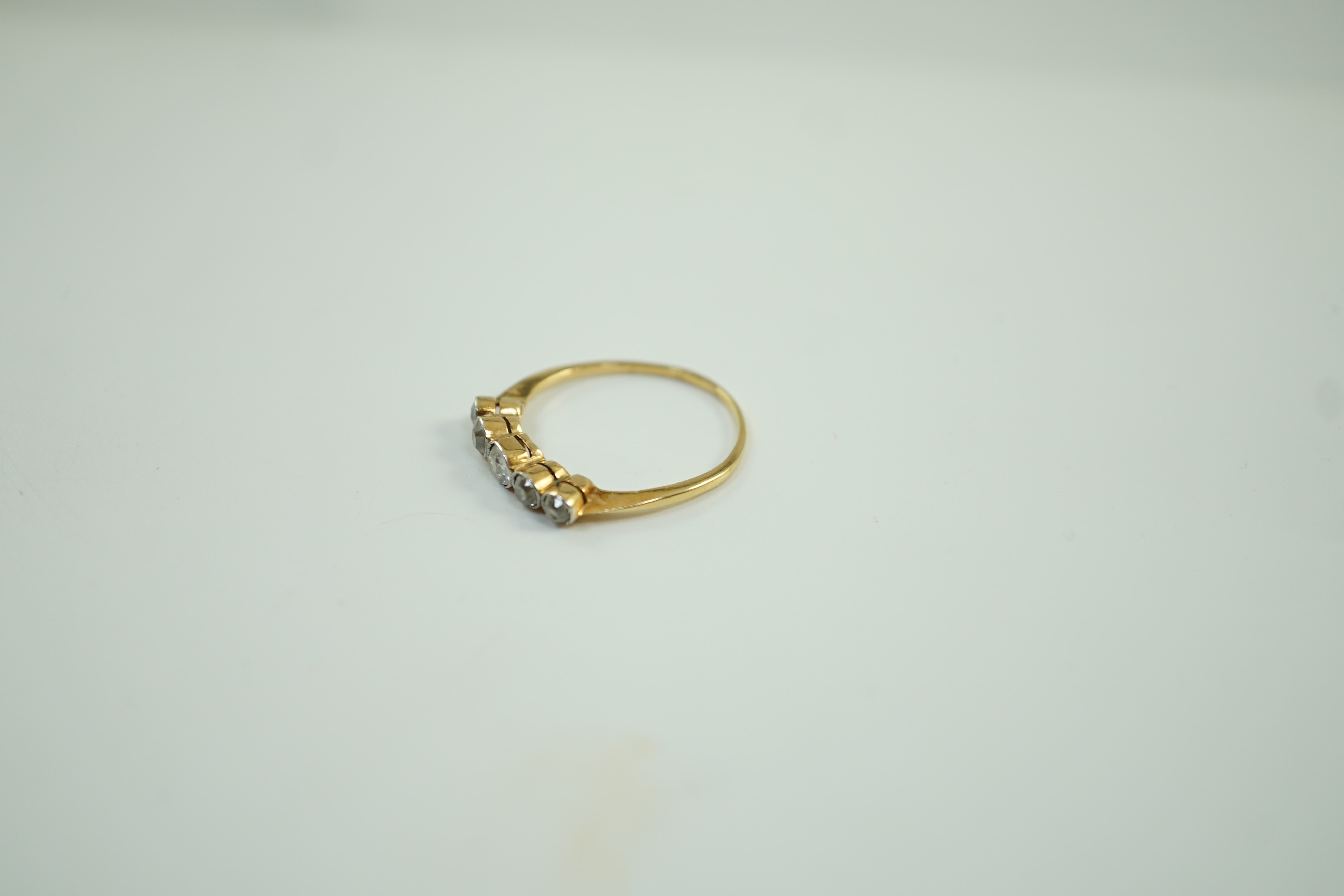 A yellow metal and graduated collet set five stone diamond half hoop ring, size V, gross weight 2.6 grams.